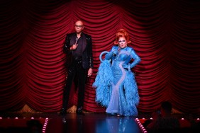 RuPaul in a black suit standing in front of red curtain at Drag Race Live, along with Ginger Minj who is wearing a blue dress